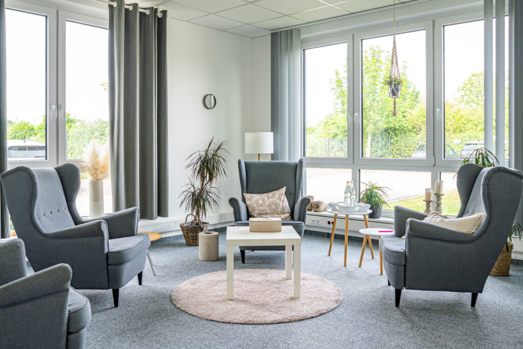 Geräumiger Gruppenraum der JUNA GbR in Herten mit grauen Ohrensesseln und großen Fenstern für systemische Familientherapie, Gruppenarbeit und Jugendhilfeleistungen