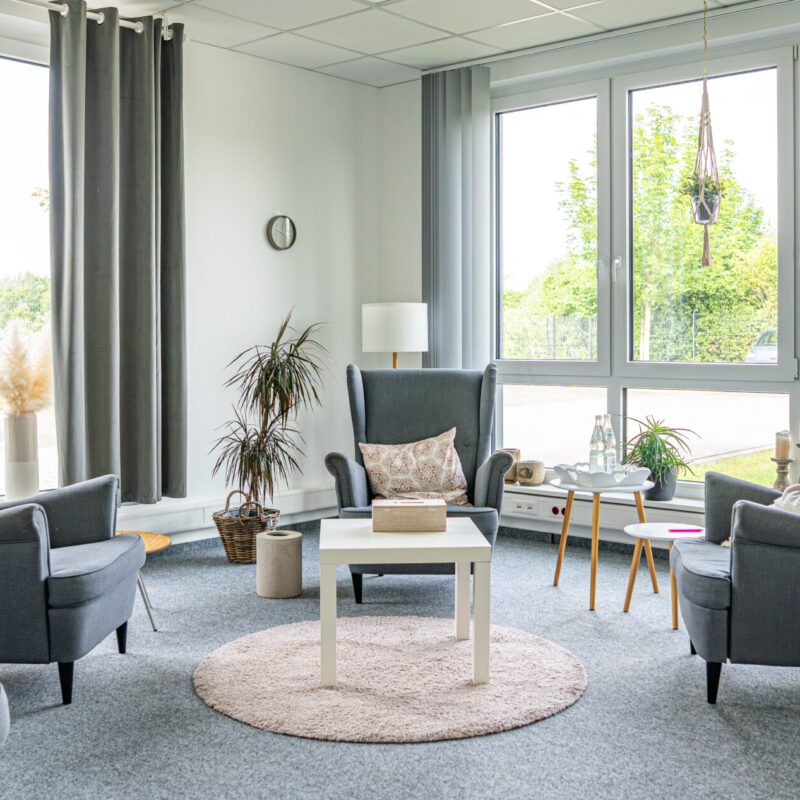 Geräumiger Gruppenraum der JUNA GbR in Herten mit grauen Ohrensesseln und großen Fenstern für systemische Familientherapie, Gruppenarbeit und Jugendhilfeleistungen
