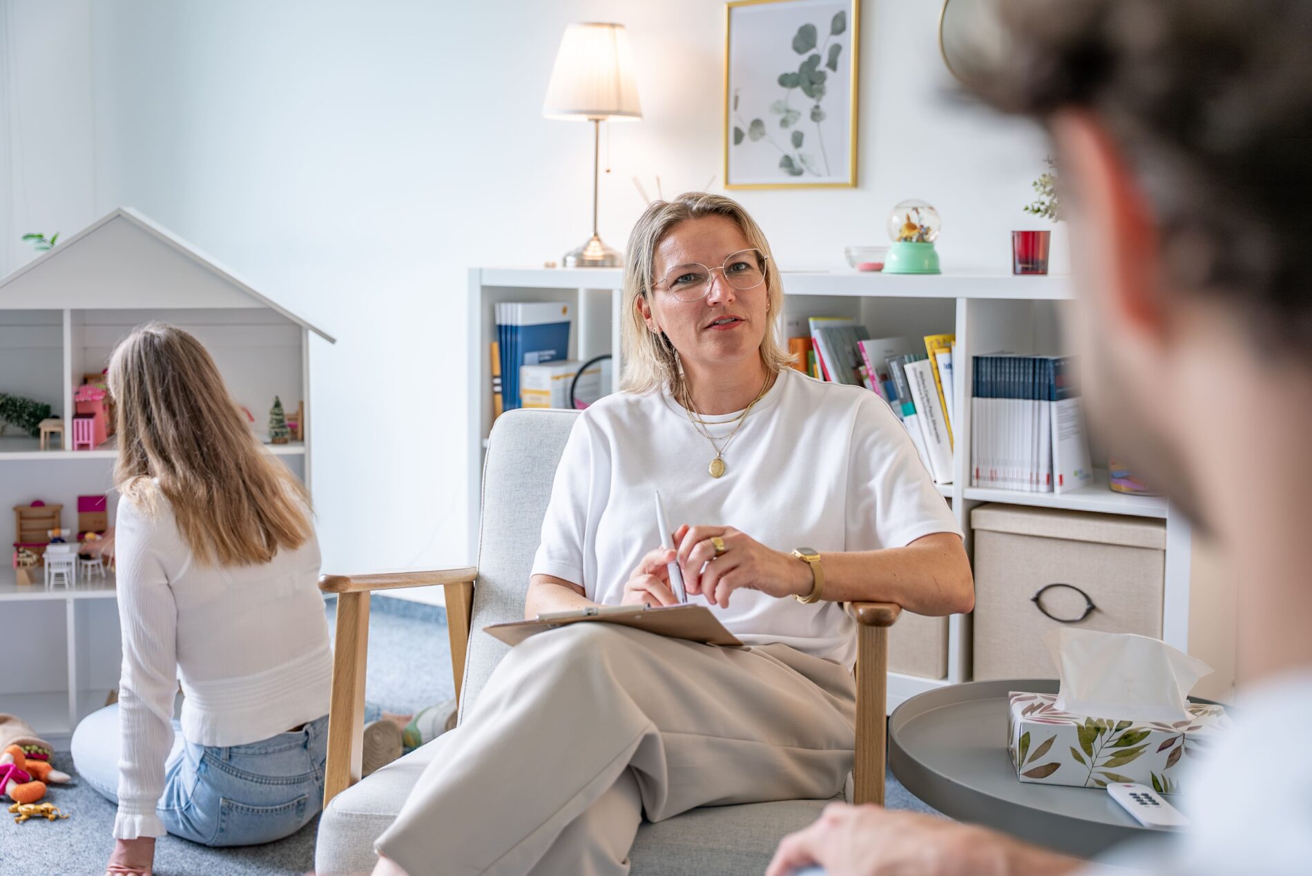 Therapeutin der JUNA GbR Herten im systemischen Familiengespräch mit Elternteil während Kind spielt — integrative Familientherapie für Kinder, Eltern und Familien in Herten
